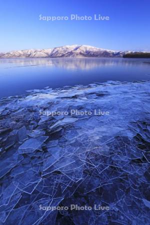 朝の屈斜路湖の岸に寄せられた氷と藻琴山