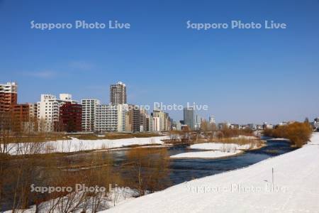 雪解けの豊平川とマンション群